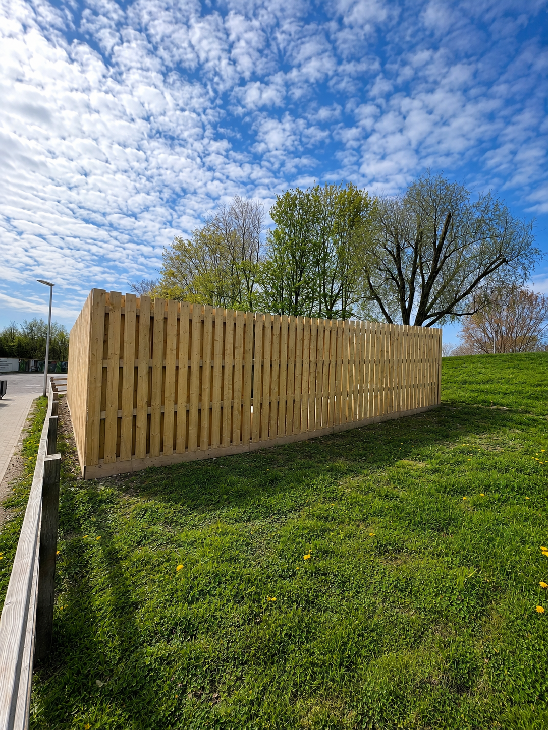 Timber hit and miss fence panel forming a boundary on grass with trees and blue sky behind