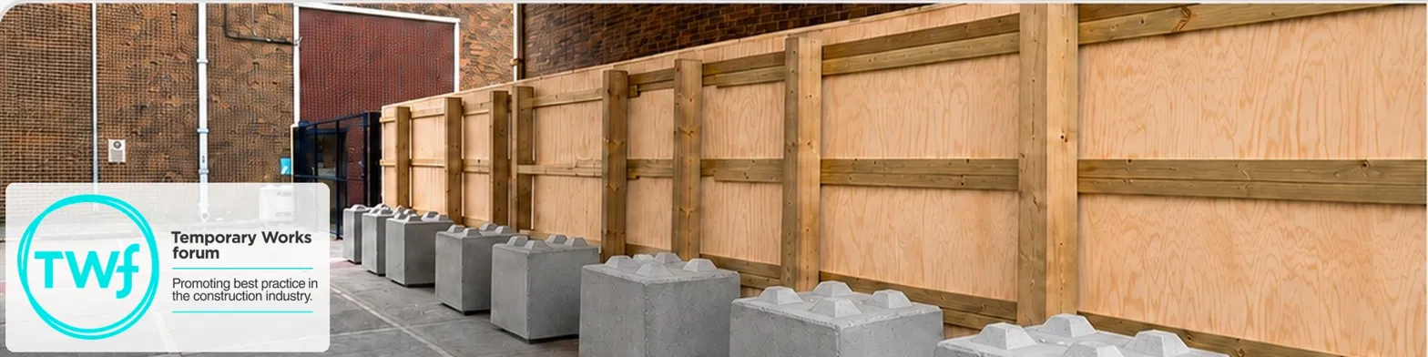 Timber hoarding secured with a row of concrete ballast blocks along a site boundary, with a Temporary Works Forum logo overlay