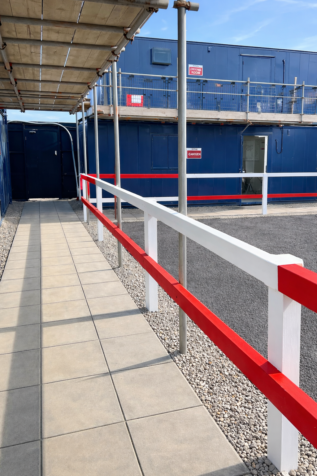Red and white timber knee rail alongside a covered walkway between site cabins