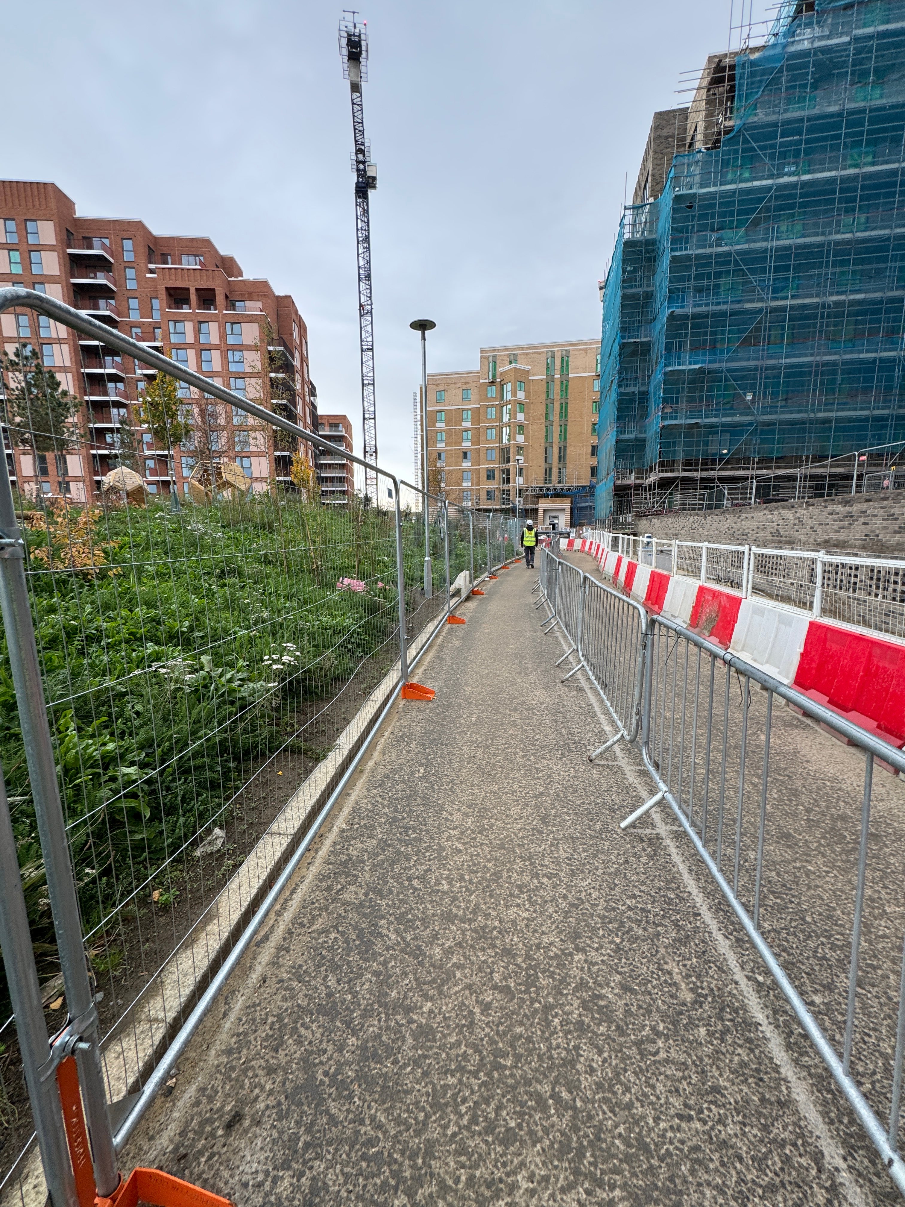Segregated pedestrian walkway on a construction site with mesh fencing and red and white barriers